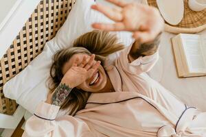 Söt leende kvinna avkopplande på Hem på säng i morgon- i pyjamas foto