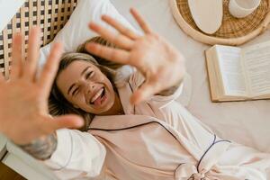 Söt leende kvinna avkopplande på Hem på säng i morgon- i pyjamas foto