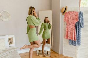 ung Söt kvinna i grön klänning påfrestande på stil trend klänning ser i spegel foto