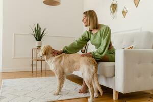 ung eleganta leende kvinna i grön sommar klänning petting hund på Hem foto