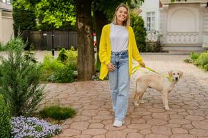 Lycklig leende kvinna i gul Tröja gående på henne hus med en hund gyllene retriever foto
