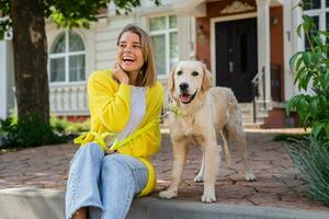 Lycklig leende kvinna i gul Tröja gående på henne hus med en hund gyllene retriever foto