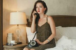 ung skön kvinna Sammanträde på säng i hotell rum foto