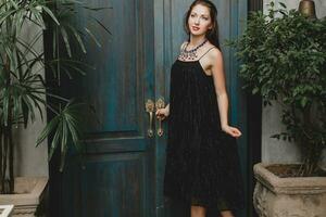 porträtt av ung attraktiv kvinna i eleganta svart klänning Framställ på tropisk villa foto