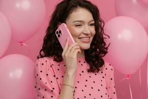 Söt ung kvinna Framställ isolerat på rosa studio bakgrund med rosa luft baloons och smartphone foto