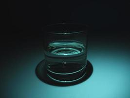 halvfullt glas med vatten i mörkret. svart bakgrund foto
