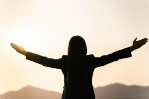 glad affärskvinna som sprider armar och tittar på bergsilhouetten. affärsframgångskoncept, frihetskänslor foto