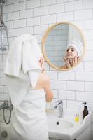 ung kvinna i vit handduk applicera fuktgivande olja på ansiktshuden. foto