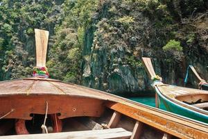 långstjärtade båtar förtöjda för att betjäna turister på turkosa stränder i Koh Phi Phi i Thailand. genom att vända fören mot klippiga berg är denna kust sommarmål för resor och resor. foto
