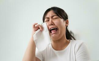 porträtt av en ledsen asiatisk kvinna gråt våtservetter henne tårar med en vävnad papper handduk. foto