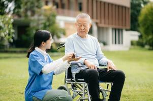 äldre asiatisk senior man på rullstol med asiatisk försiktig vårdgivare. amning Hem sjukhus trädgård begrepp är gående i de trädgård. till hjälp och uppmuntra. foto