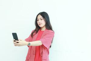 porträtt av skön asiatisk kvinna bär röd utrusta ser på mobil telefon med tänkande uttryck foto