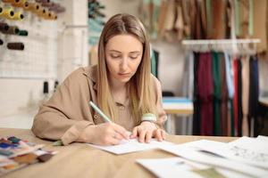ung kvinnlig modedesigner ritar skiss med modell sitter på hennes kontor.