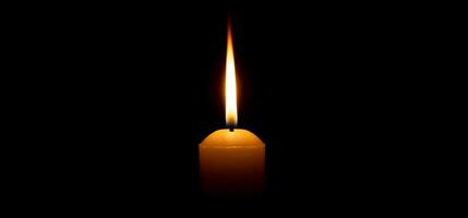 enda brinnande ljus flamma eller ljus lysande på en stor gul ljus på svart eller mörk bakgrund på tabell i kyrka för jul, begravning eller minnesmärke service med kopia Plats. foto