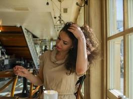 en lockighårig kvinna sitter vid ett bord på ett kafé och rätar ut håret