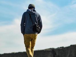 en man i hujtröja och stickad hatt går längs vägen till fästningen mot bakgrund av tornet och den blå himlen foto