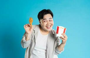 porträtt av asiatisk man äter snabb mat på blå bakgrund foto