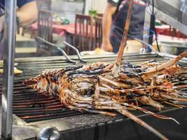 grillad hummer på ett galler över elden vid fiskmarknaden för skaldjur, grillade räkor och hummer på grillen på natten marknaden i Hua Hin, Thailand foto