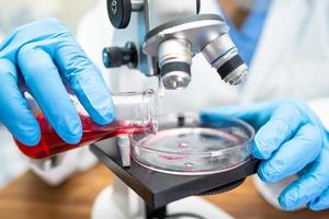 asiatisk forskare biokemiker eller mikrobiolog arbetar forskning med ett mikroskop i laboratorium. för att skydda utbrott av coronavirus covid19, bakterier och bakterier. foto