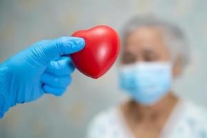 läkare som håller rött hjärta med asiatisk äldre eller äldre gammal damkvinnapatient som bär en ansiktsmask på sjukhus för att skydda infektion covid-19 coronavirus.