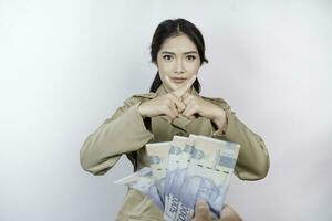 en allvarlig ung regering arbetstagare kvinna är bär kaki enhetlig gestikulerar avslag till kontanter pengar i indonesiska rupiah isolerat förbi vit bakgrund foto