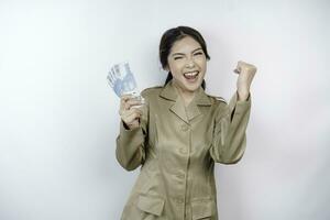 en framgångsrik ung regering arbetstagare kvinna är bär kaki enhetlig innehav kontanter pengar i indonesiska rupiah isolerat förbi vit bakgrund foto
