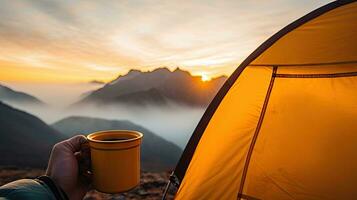 camping innehav en kopp i ett öppen gul tält med en dimmig berg belyst förbi naturlig ljus. foto