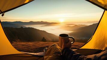 camping innehav en kopp i ett öppen gul tält med en dimmig berg belyst förbi naturlig ljus. foto