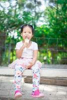 asiatisk liten flicka som äter en glass utomhus med naturligt ljus oskärpa bakgrund foto