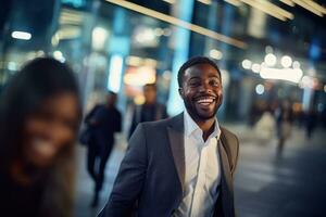 porträtt av Lycklig afrikansk amerikan affärsman gående på gata på natt, leende svart chef i modern stad omgiven förbi suddig människor. foto