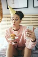 kvinna blåser ut de ljus på de födelsedag kaka och framställning en selfie foto