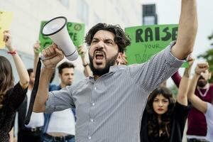 man innehav megafon skrikande med demonstranter på gata foto