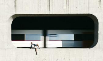 spanien, dragona, avslappnad ung man i nisch av en betong vägg med rör på sig tåg i bakgrund foto