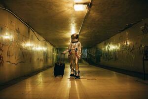 spaceman i de stad på natt i tunnel med rullande resväska foto