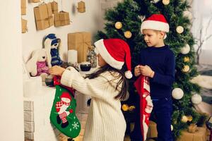 barn öppning jul presenterar. barn sökande för godis och gåvor i första advent kalender på vinter- morgon. dekorerad jul träd för familj med barn. liten flicka och pojke i xmas pyjamas. foto