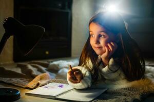 en Söt liten flicka läsning en bok på de golv under de lampa. barn och utbildning. foto