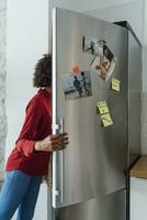 hungrig kvinna stående i kök, sökande henne kylskåp foto