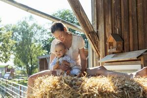 Lycklig mor och liten dotter Sammanträde i sugrör i en ladugård foto