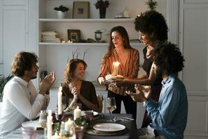 vänner förvånande ung kvinna med en födelsedag kaka med brinnande ljus foto