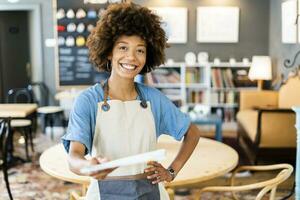 Lycklig kvinna ägare ger meny medan stående med hand på höft på kaffe affär foto