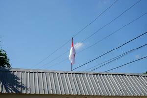 de röd och vit indonesiska flagga är flygande mot en bakgrund av blå himmel och kablar foto