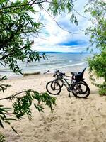 två berg Cyklar på en sandig strand. blå himmel, vit moln och grön träd. foto