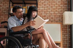 barnbarnet satt på den gamla asiatiska farfarens knä i rullstol. foto