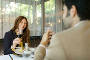 leende kvinna med glas av röd vin ser på man i en restaurang foto