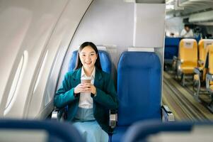 porträtt av framgångsrik asiatisk affärskvinna eller entreprenör i en formell kostym på ett flygplan Sammanträde i företag klass använder sig av en telefon, dator bärbar dator. resa i stil, arbete med nåd. foto