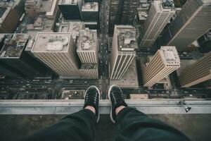 äventyrlig urban explorer Sammanträde på skyskrapa avsats med gymnastikskor hängande över kant foto