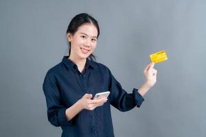 ung asiatisk tjej som visar plastkreditkort medan du håller mobiltelefonen