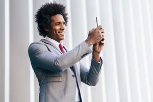 svart affärsman som använder en smartphone nära en kontorsbyggnad foto