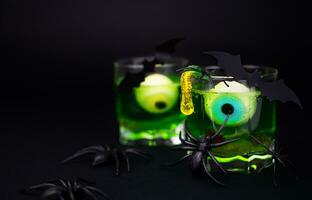 kuslig grön cocktails med ögon, gelé maskar i en glas och spindlar och fladdermöss på en svart bakgrund. festlig halloween fest. kopia Plats. närbild. selektiv fokus. foto