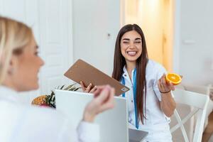 läkare nutritionist, dietist och kvinna patient på samråd i de kontor. ung leende kvinna dietist i de samråd rum. dietist skrivbord med friska frukt och mätning tejp. foto